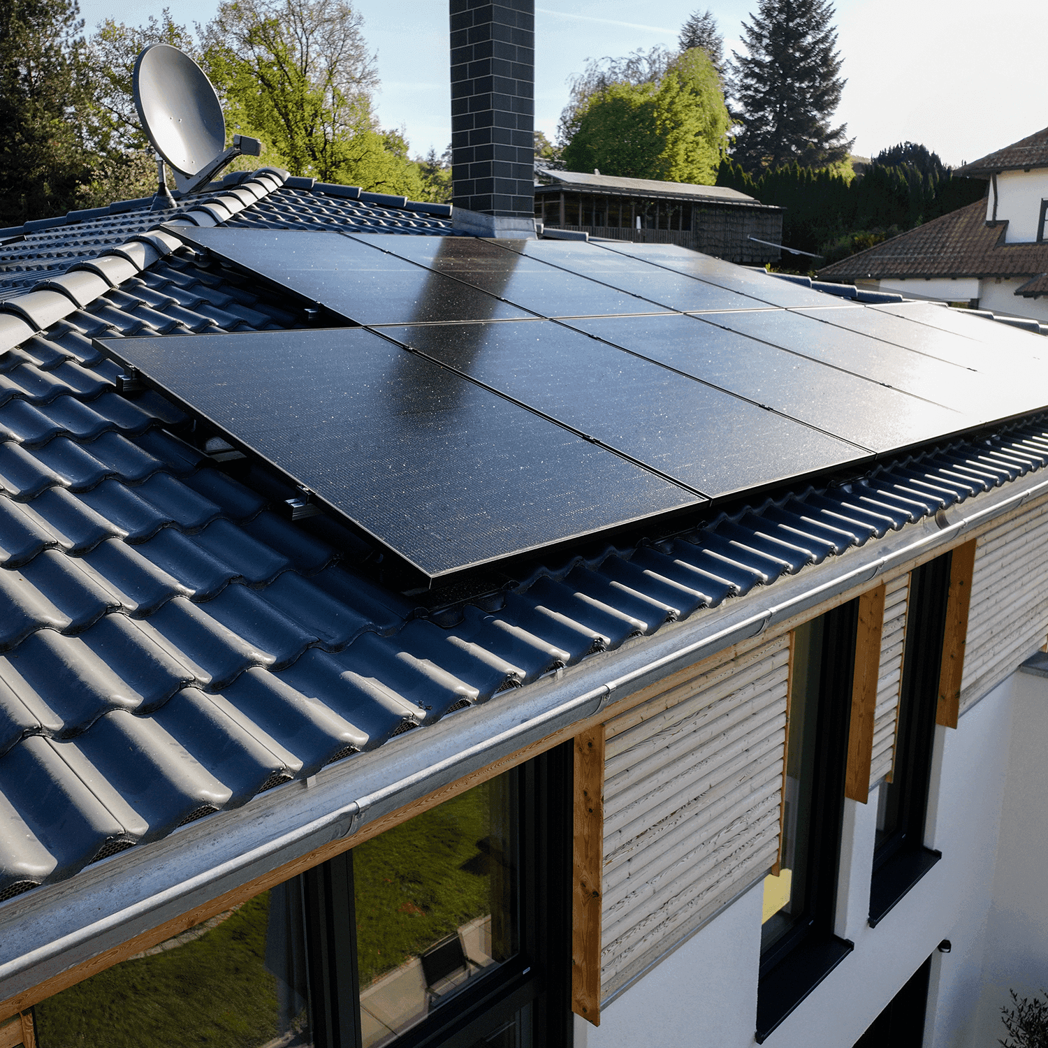 Modernin talon katolla on aurinkopaneelit, ja sitä ympäröivät puut. Katolla on myös savupiippu ja satelliittiantenni.