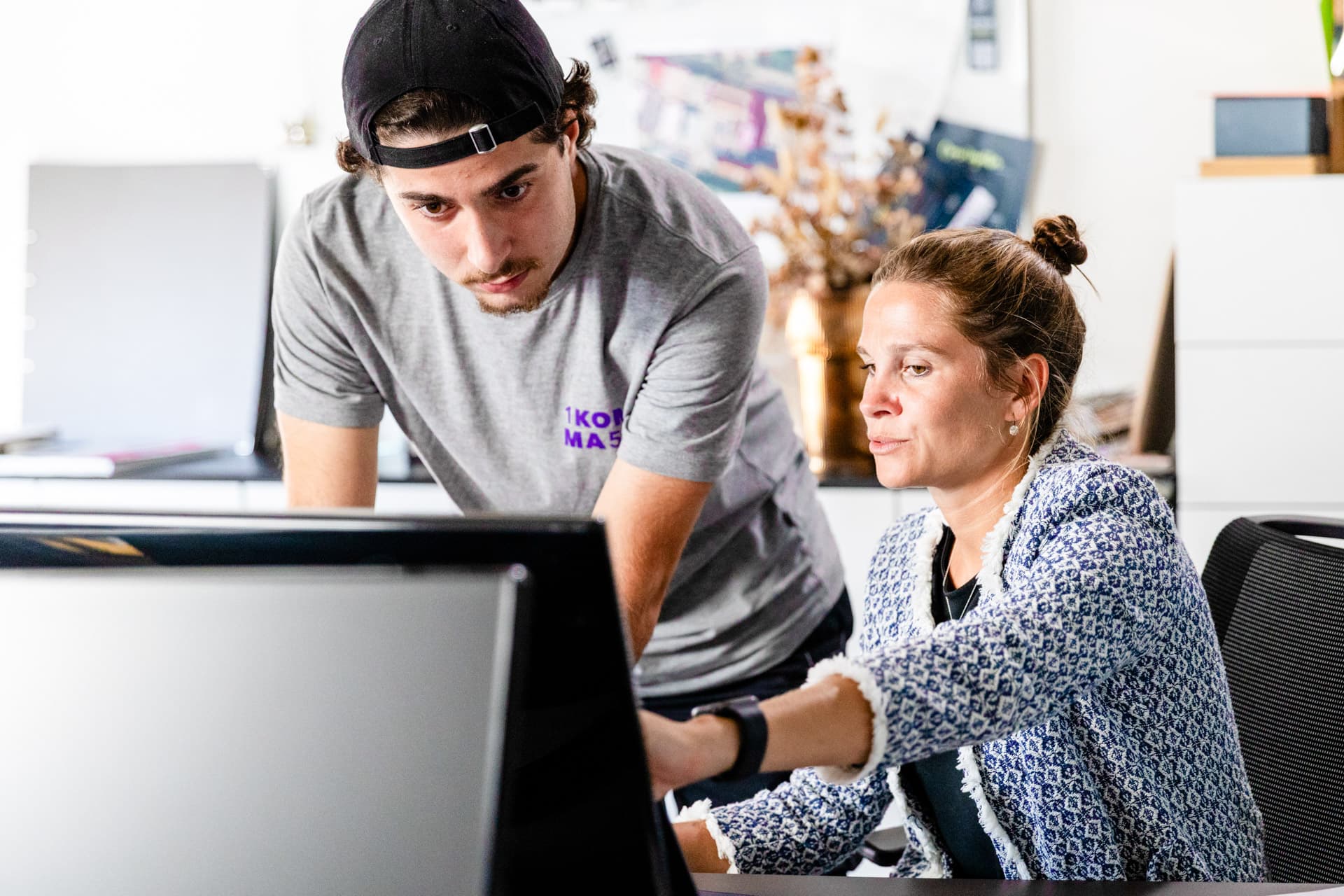 Kolme ihmistä 1KOMMA5°-näyttelytilassa, joka on sisustettu violetilla valaistuksella. Konsultti esittelee älypuhelinta kahdelle asiakkaalle – miehelle ja naiselle – keskustellen sen ominaisuuksista.