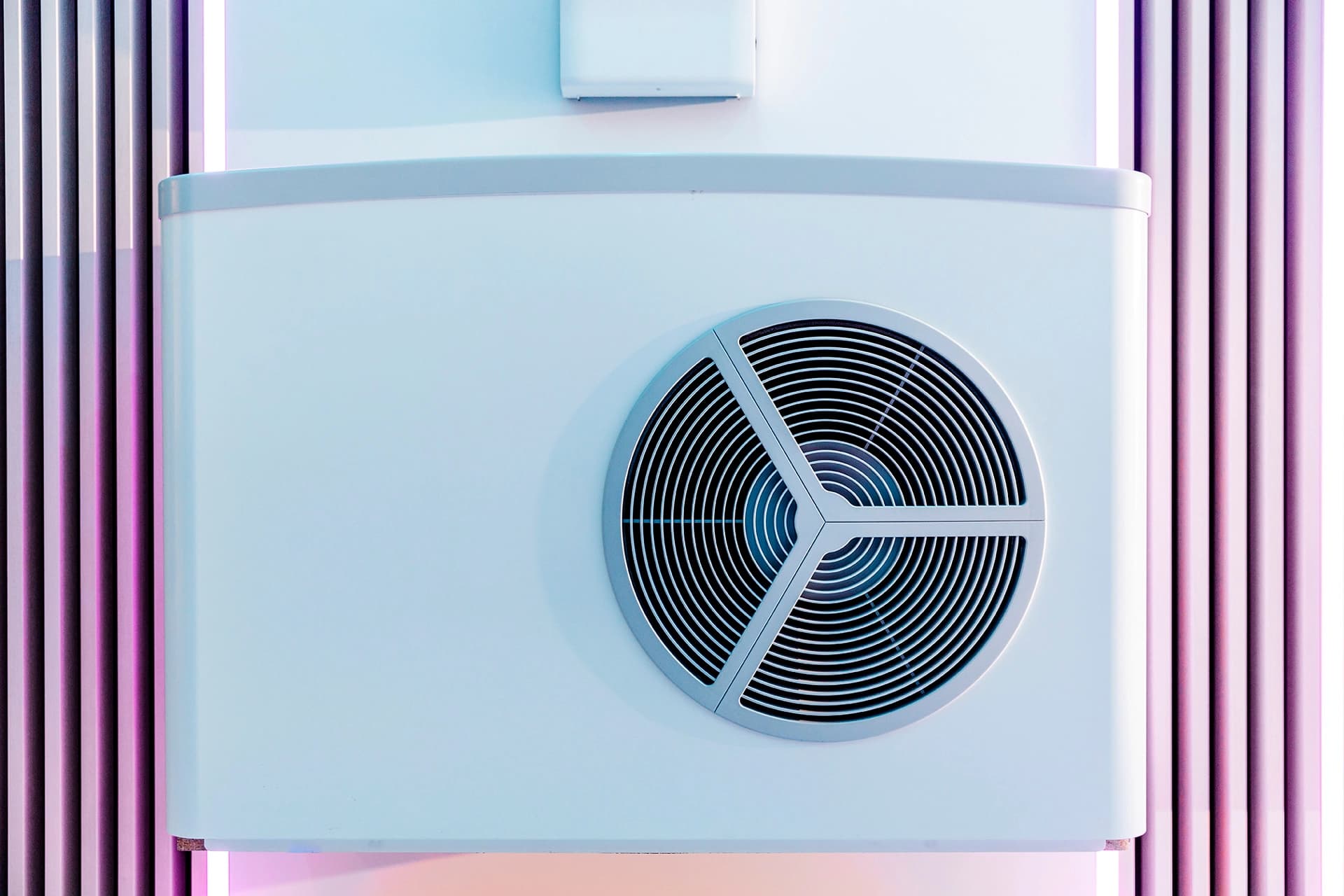 Moderni lämpöpumppuyksikkö, jossa on pyöreä ilmanvaihtoaukko, asennettuna seinälle, jossa on pystysuuntainen raidallinen design, valaistuna pehmeällä pinkillä ja sinisellä valolla.