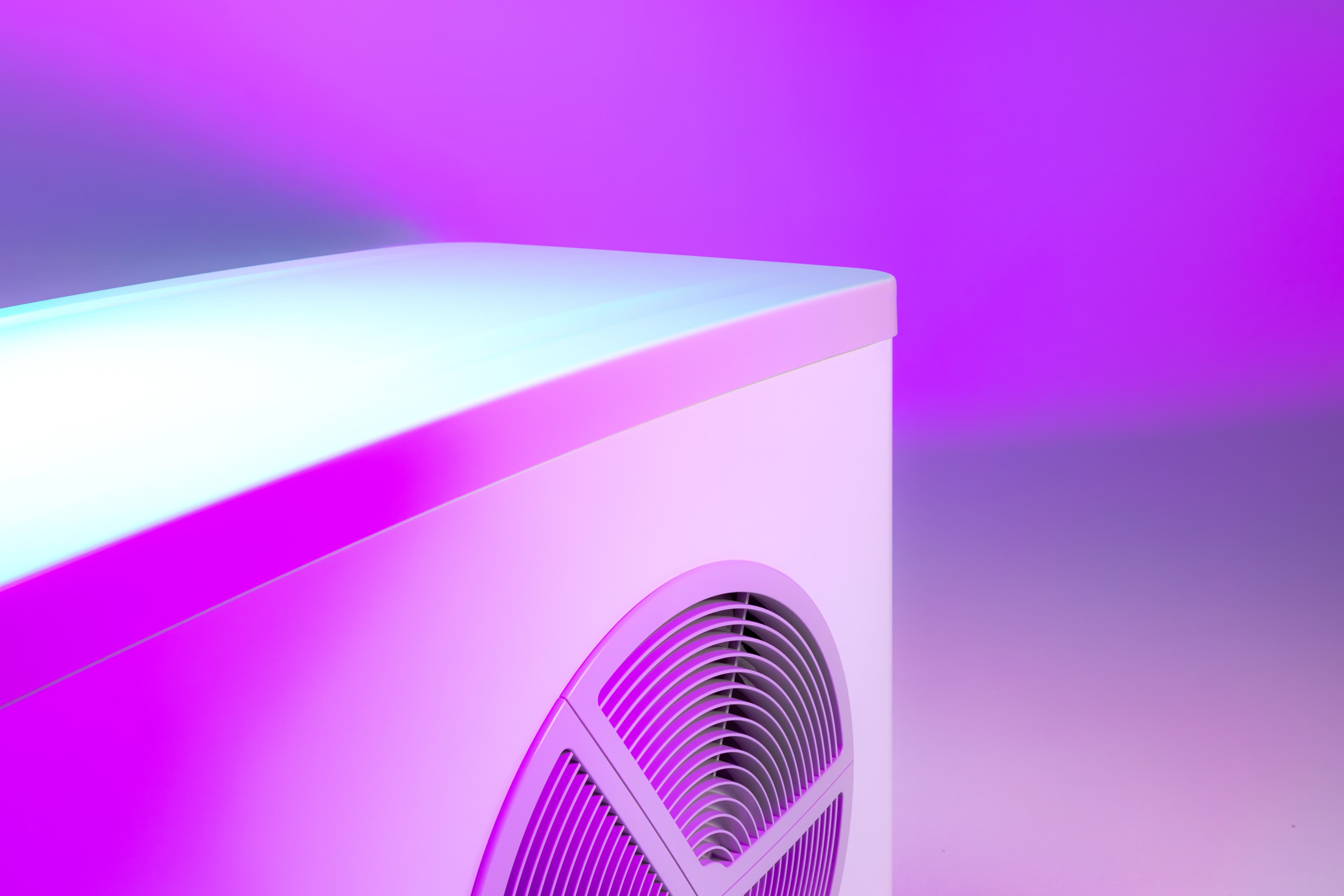 Lähikuva modernista lämpöpumpusta, jossa on pyöreä ilmanvaihtoaukko, valaistuna pinkillä ja violetilla valolla.